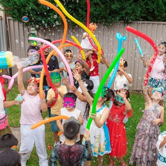Children reaching for bubbles and balloons at a backyard party